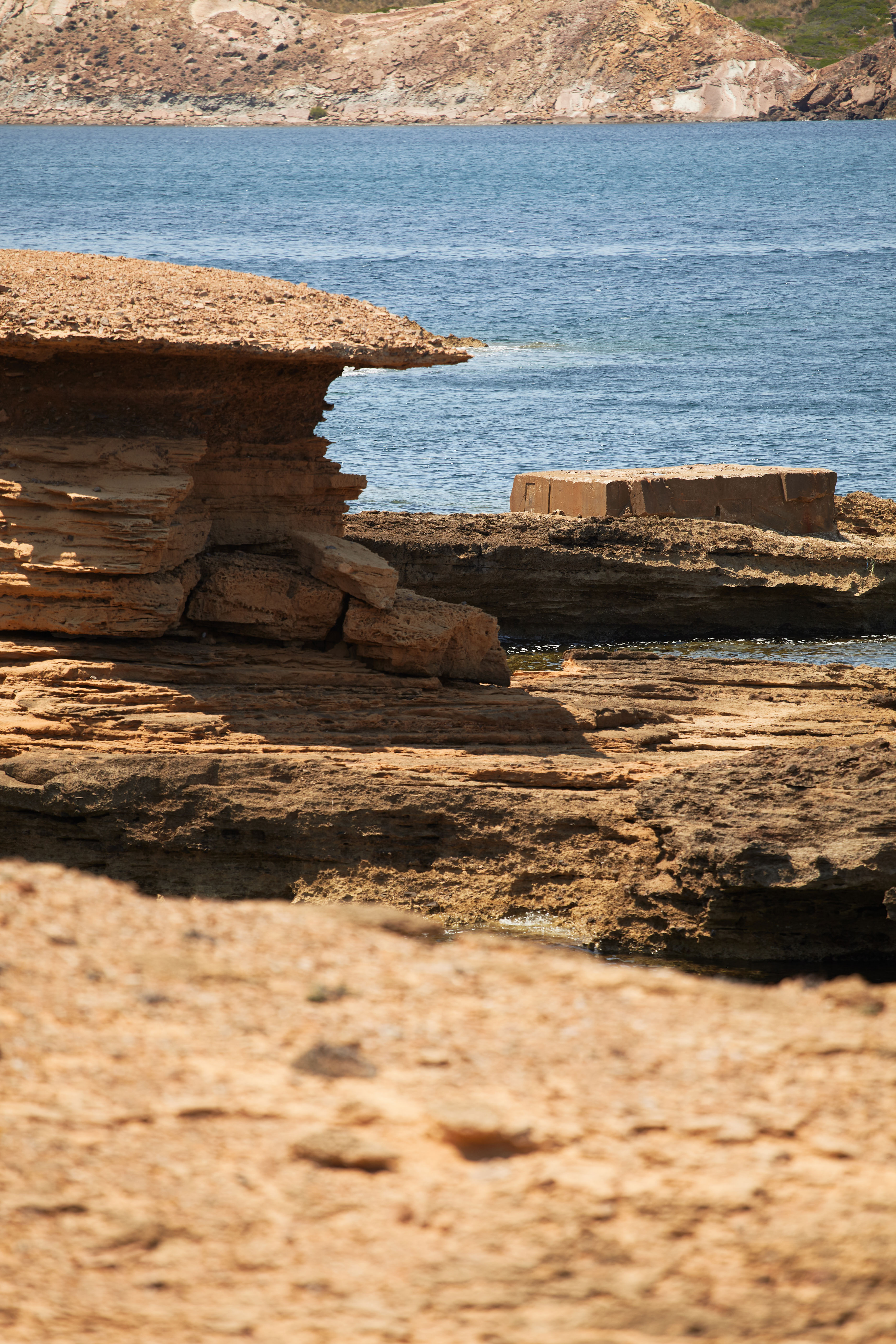 Vista de Cala Pregonda con arena dorada, rocas rojizas y mar azul en la costa norte de Menorca