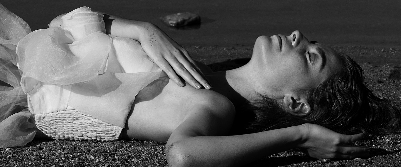 Modelo femenina en blanco y negro recostada sobre la orilla de un embalse.