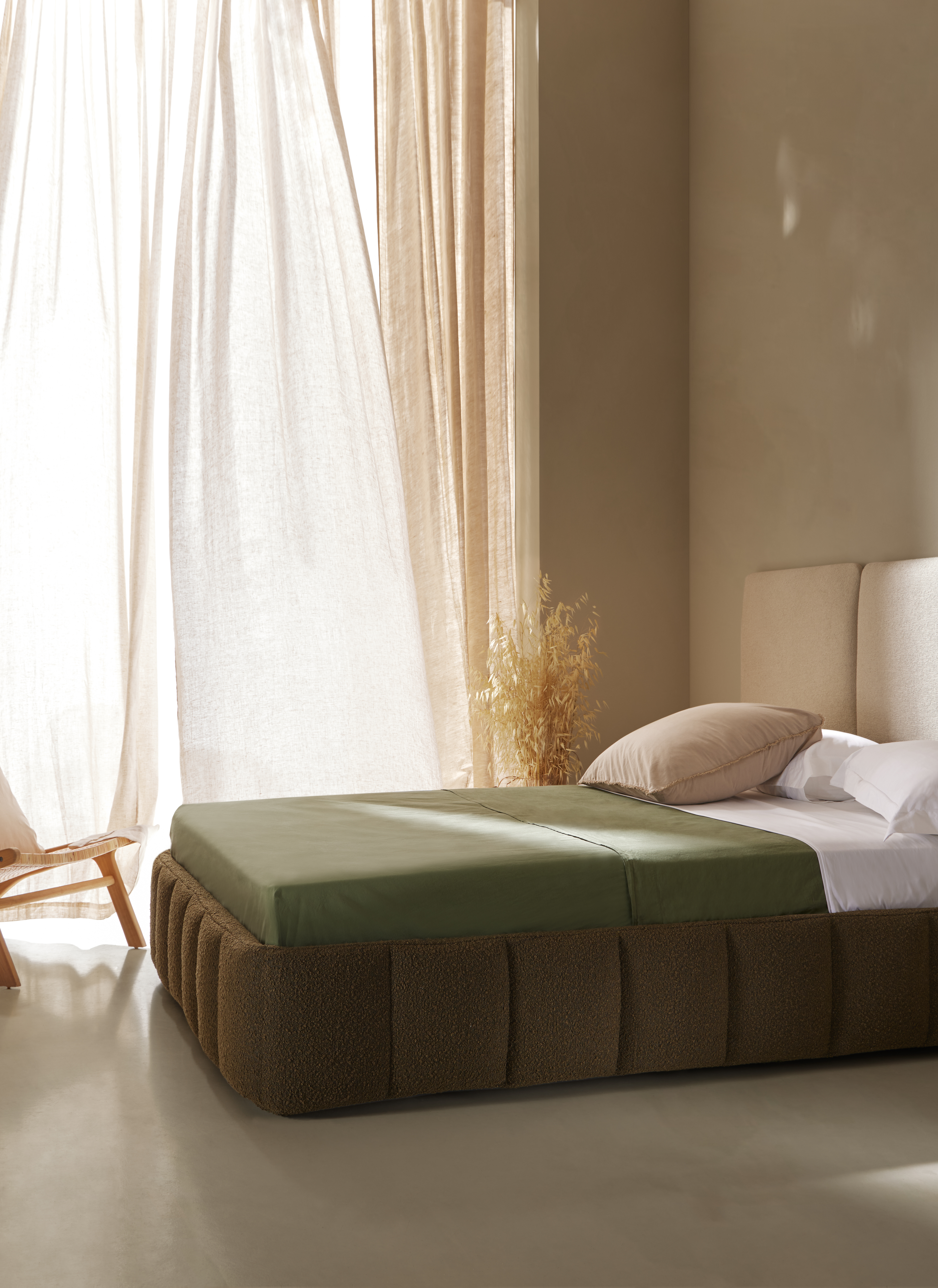 Dormitorio contemporáneo con cama tapizada, cabecero modular y luz natural filtrándose sobre superficies textiles en tonos neutros
